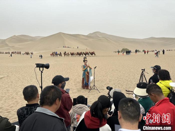 圖為2023年4月底，敦煌大漠“逐舞者”奧楠在鳴沙山月牙泉景區(qū)視頻直播，吸引游人圍觀?！●T志軍 攝